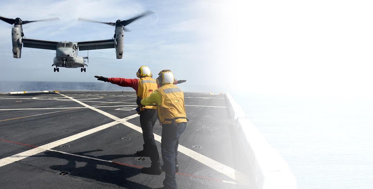 两个人使用军事卫星通信与一架MV-22在海上降落在一艘航空母舰上进行通信